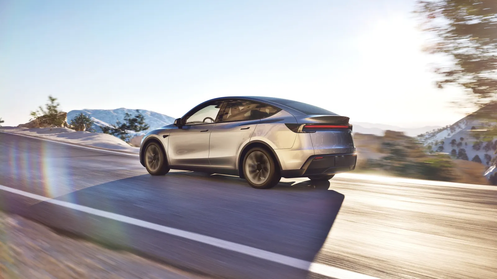Tesla Model Y plateado circulando por una carretera de montaña con nieve al atardecer