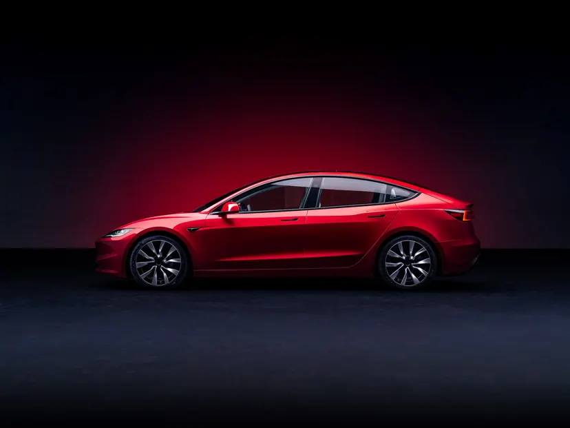 Tesla Model 3 rojo de perfil sobre fondo oscuro con un halo de luz roja