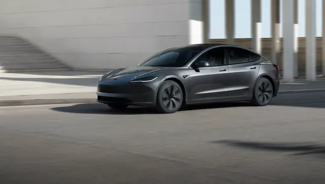 Tesla Model 3 gris circulando por una calle junto a un edificio con columnas